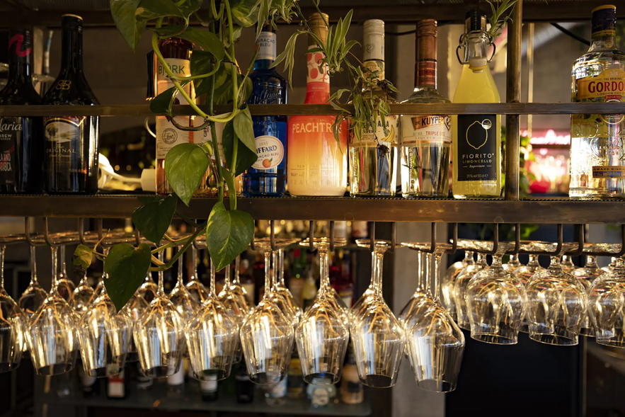Assorted liquor bottles and hanging wine glasses at The Greenhouse food hall in Hveragerdi.