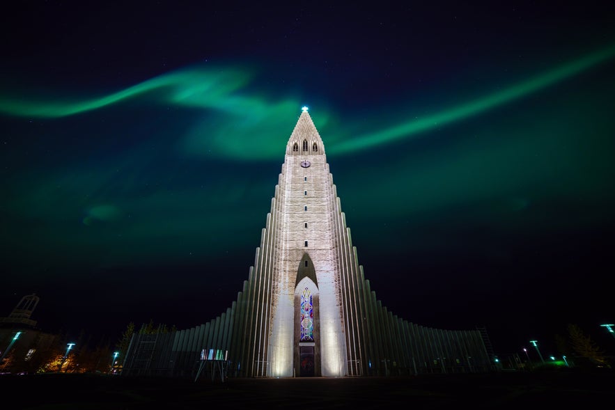 Northern lights stream across the night sky above Hallgrimskirkja church in Reykjavik, Iceland, highlighting its striking tower.