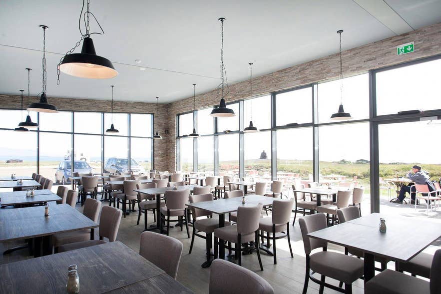 Salle spacieuse du Snjófell Restaurant à Snaefellsnes, en Islande, avec de grandes fenêtres donnant sur les falaises et le littoral.