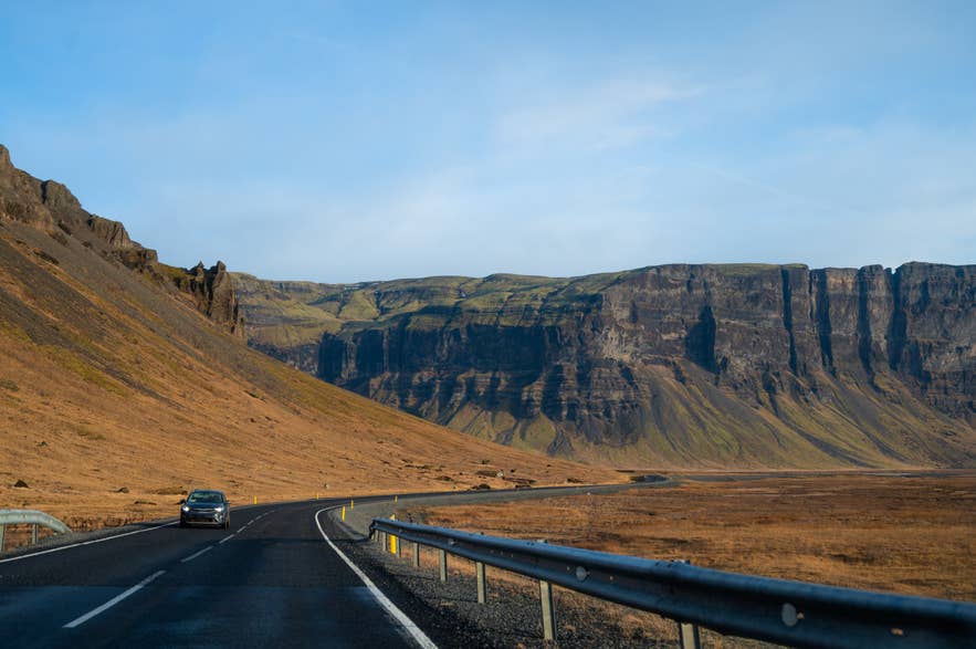 Car driving on a winding road along dramatic cliffs on Iceland’s South Coast.