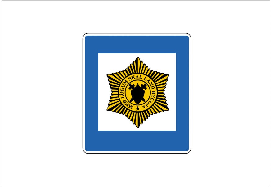 An Icelandic road sign with a white background, blue border, and a yellow-and-black badge in the center indicates a police station.