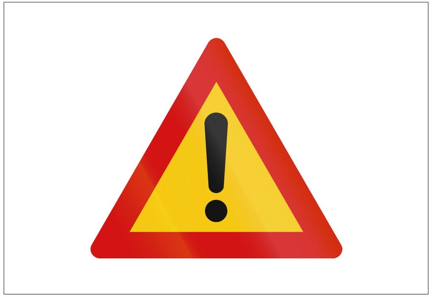 A yellow triangular road sign with a red border and black exclamation mark warns of a bumpy gravel road ahead. 