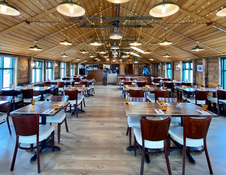 Eleganckie wnętrze restauracji Pakkhus w Hofn, stylowy wystrój, ciepłe oświetlenie i nakryte stoły.