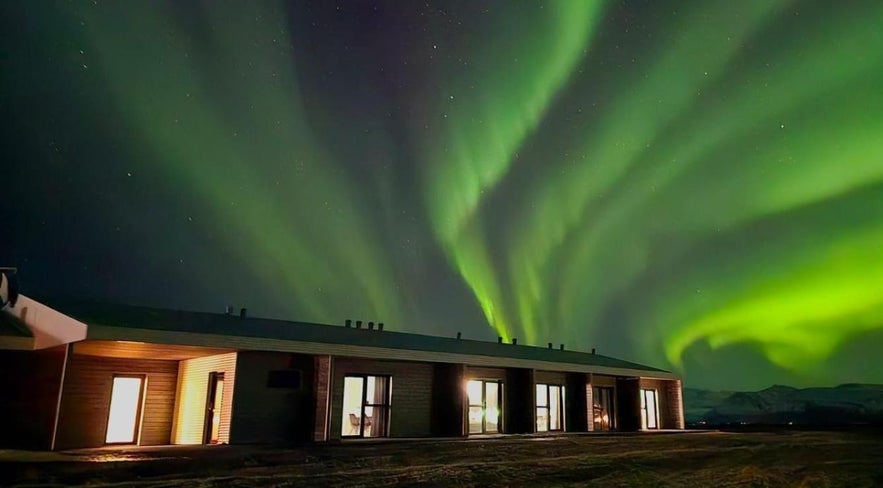 Seljavellir Guesthouse near Höfn, Iceland, with the northern lights glowing in the sky above the mountains.