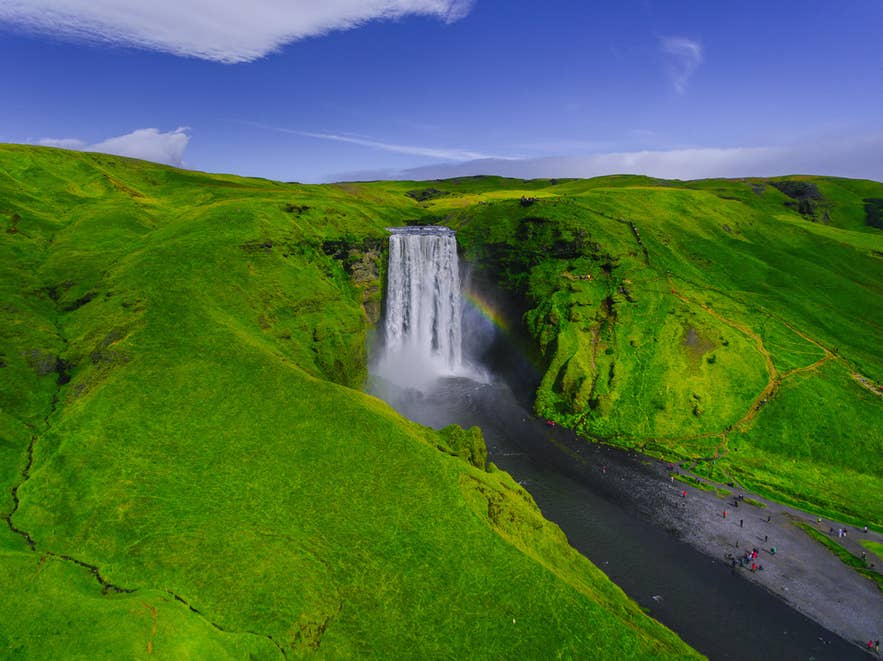 Dramatischer Fall des Skogafoss-Wasserfalls und sattgrüne Umgebung beim Drohnenfliegen in Island. Dramatischer Fall des Skogafoss-Wasserfalls und sattgrüne Umgebung beim Drohnenfliegen in Island.