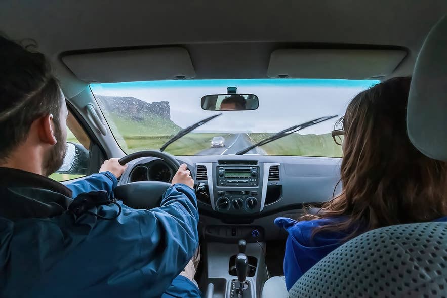 A couple driving a rental car along a scenic road in Iceland, representing the freedom of a self-drive tour.