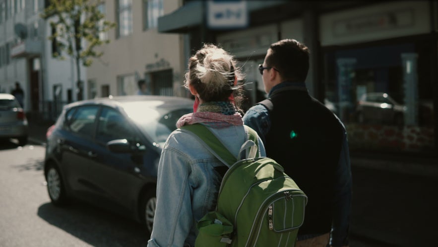 Woman and man walking in downtown Reykjavik on a sunny day, one wearing a green backpack.