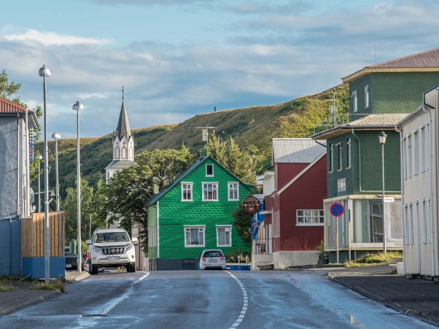 Colorful street view in Sauðárkrókur, North Iceland, featuring traditional Icelandic houses and a church steeple with grassy hills in the background.
