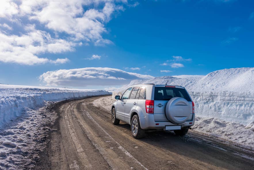 Rijden in IJsland over een besneeuwde bergweg bij Akureyri met een gehuurde terreinwagen met vierwielaandrijving onder een helderblauwe hemel.