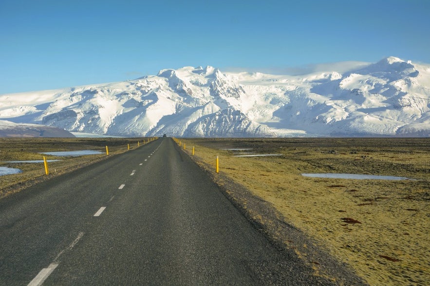 Driving in Iceland along the Ring Road with yellow roadside markers guiding travelers through open landscapes.