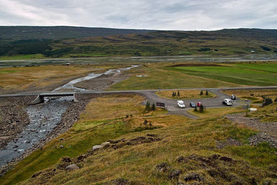 Aerial view of the car park near Hengifoss Waterfall in the Eastfjords, with a river, bridge, and sweeping green valley in the background.