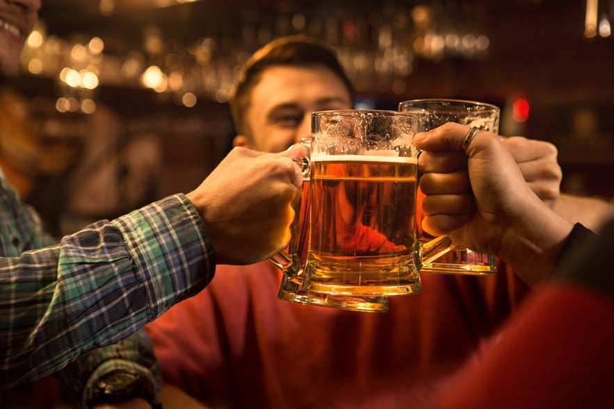 Friends clinking beer mugs during happy hour in Reykjavik, enjoying the city’s lively nightlife.
