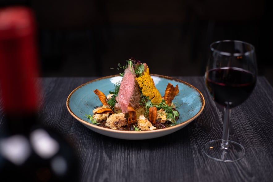 Fine dining plate of gourmet lamb with vegetables and wine pairing at Reykjavik Kitchen in Iceland.