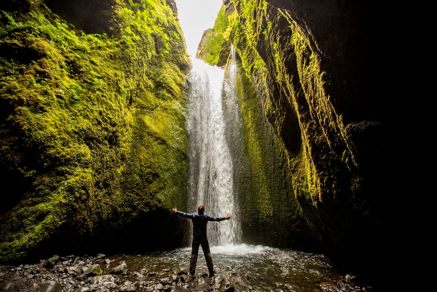 Person stands before a hidden waterfall surrounded by mossy canyon walls in Nauthusagil, South Iceland.