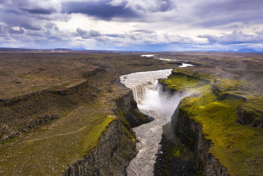 Aerial view of Jokulsargljufur canyon in north Iceland, with Dettifoss waterfall plunging into the dramatic basalt gorge under a cloudy sky.