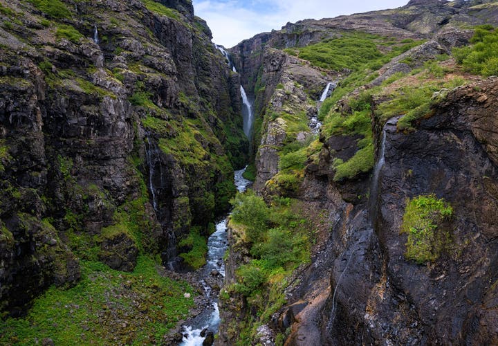 Glymur Canyon with a tall waterfall flowing between steep rocky cliffs and lush greenery in Iceland.