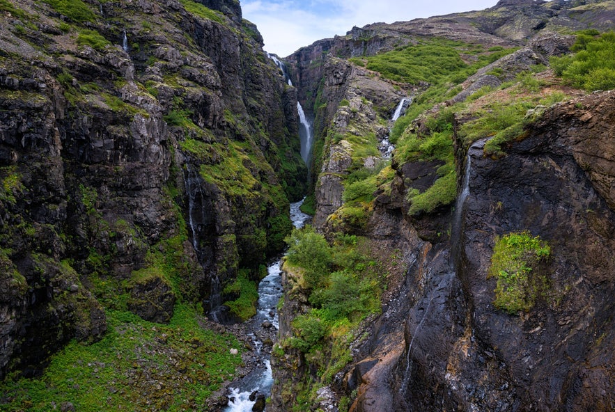 Glymur Canyon with a tall waterfall flowing between steep rocky cliffs and lush greenery in Iceland.
