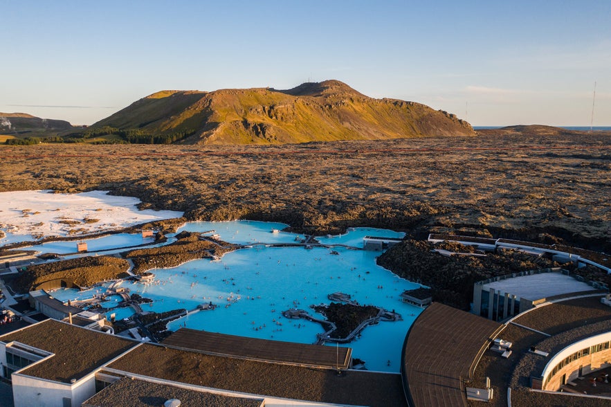 Aerial view of the Blue Lagoon in Iceland, with milky-blue geothermal waters set among black lava fields and surrounding hills.