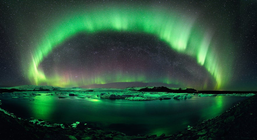 Northern lights in Iceland glowing above Jokulsarlon glacier lagoon with green aurora reflecting on icy waters.
