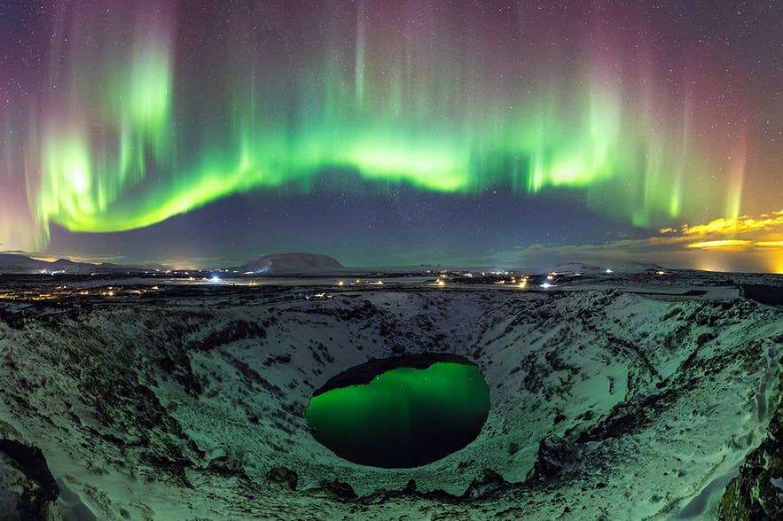 Northern lights in Iceland shining above the Kerid crater, reflecting green aurora on the volcanic lake in winter.