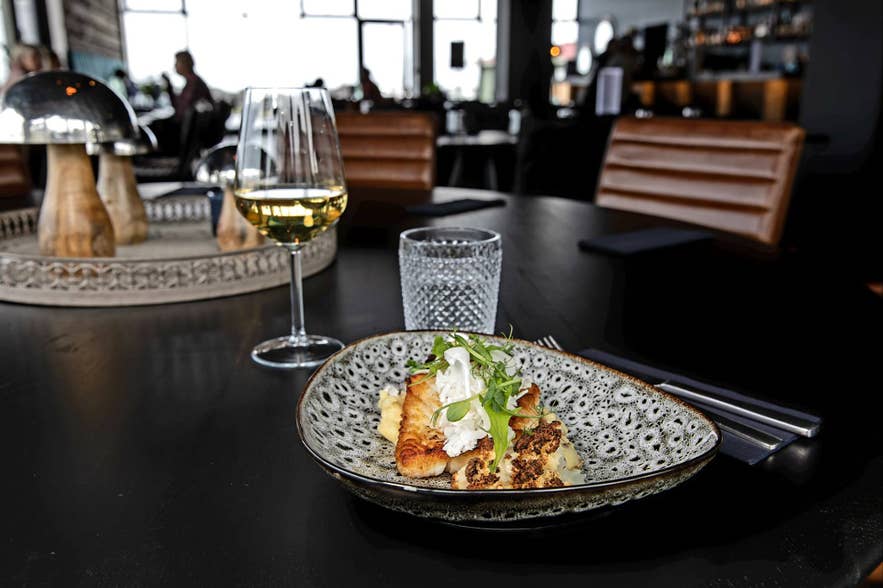 A beautifully arranged plate of food with a glass of wine on a table at Sker Restaurant, one of Iceland's finest.