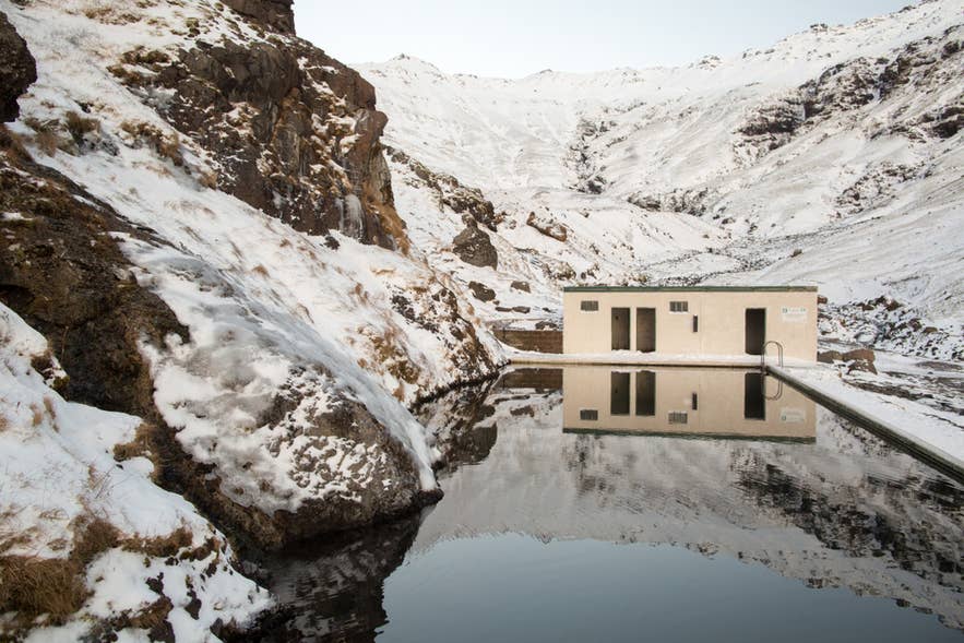 The winter setting of Seljavallalaug Pool in South Iceland is part of the hidden gems in Iceland, with hot springs in snowy mountains.