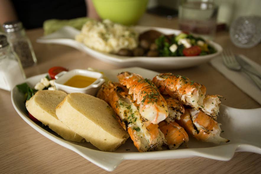 A serving of langoustine, bread, and vegetables on a fish-shaped plate.