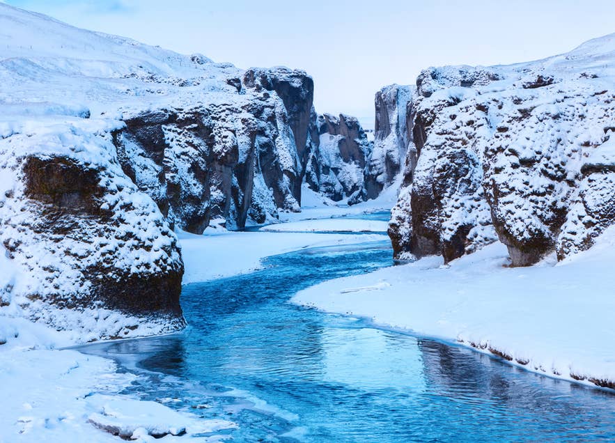 The winter landscape of Fjadrargljufur Canyon in South Iceland is among the hidden gems in Iceland, with snowy cliffs and blue water.