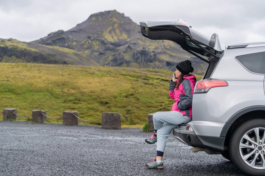 Traveler on a self-drive in Iceland sitting by car with mountain views.