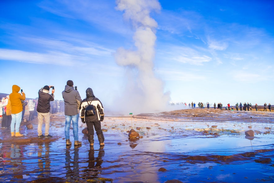 Tourists watch Strokkur geyser erupting in Iceland’s Golden Circle, shooting steam and water into the sky.