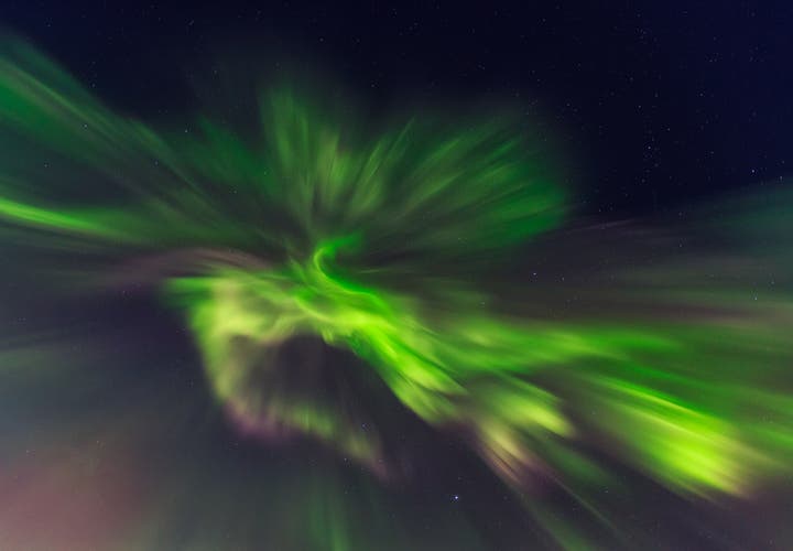 Bright green northern lights bursting across the night sky in Iceland, forming a dramatic corona pattern of light.