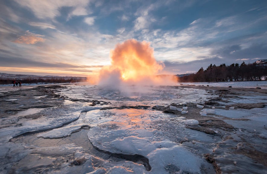 Strokkur geyser erupting at sunrise in Iceland’s Golden Circle, with steam and glowing light on the icy landscape.