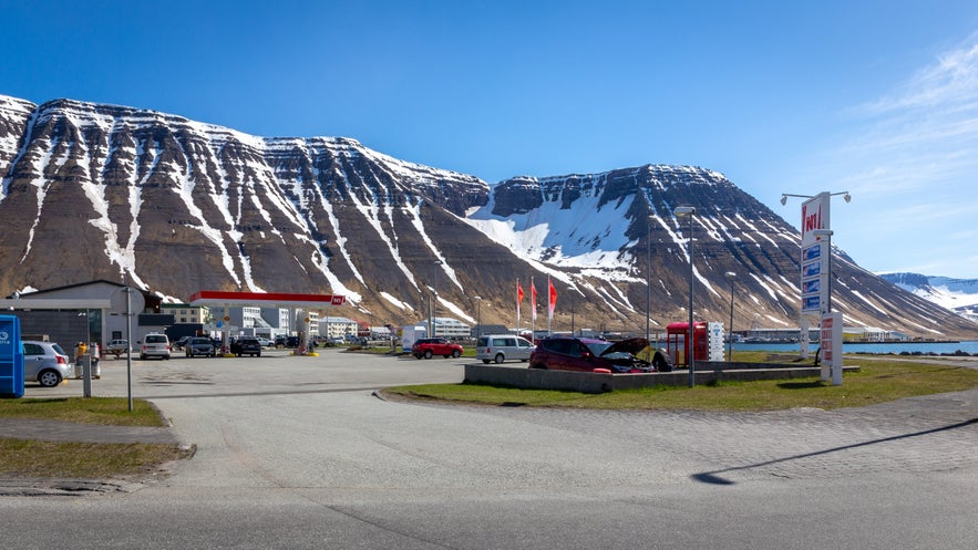 N1 gas station in Ísafjördur with dramatic snow-streaked mountains in the background under a clear blue sky
