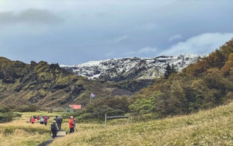 Tourists walking towards mountain huts in Thorsmork with glacier backdrop.
