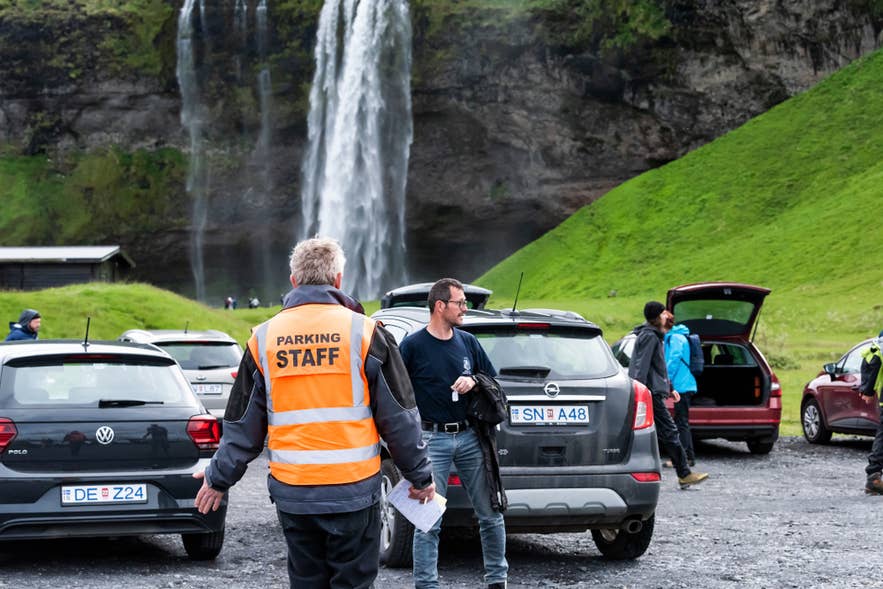 Multas de aparcamiento en Islandia aplicadas en la Cascada Seljalandsfoss con personal revisando vehículos de turistas.