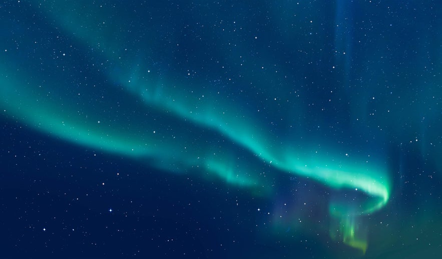 Gentle blue-green northern lights ripple across a star-filled sky, creating a soft arc of light in the darkness.