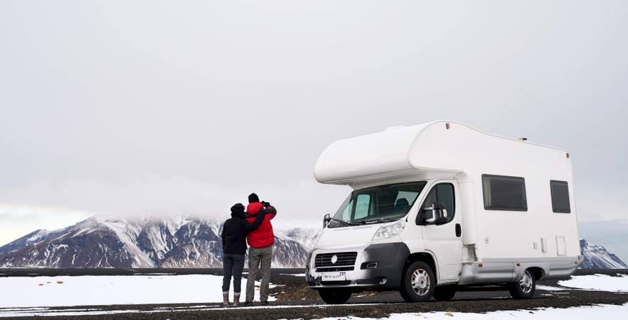 Couple avec van aménagé dans un paysage islandais enneigé, illustrant l’aventure en road trip et les hébergements uniques en Islande.