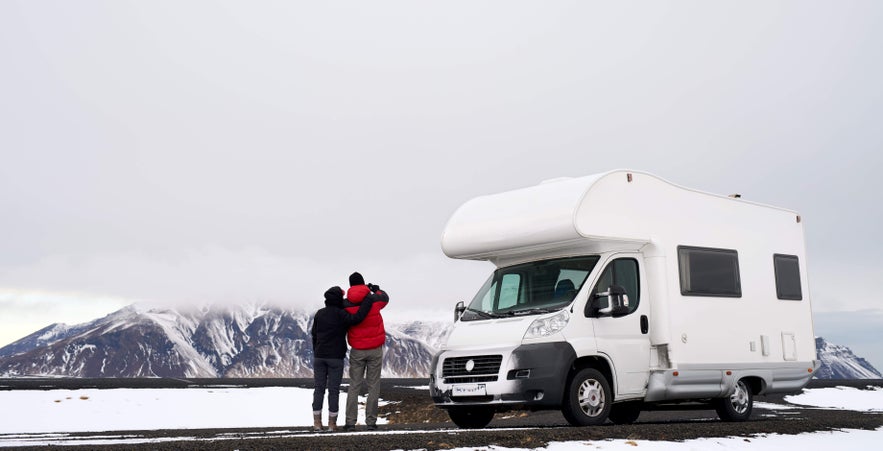 Couple with campervan in snowy Icelandic landscape, highlighting road trip adventures and unique places to stay in Iceland.