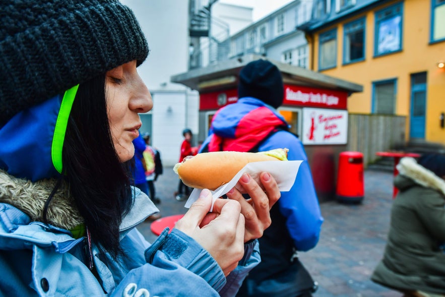 Traveler enjoying Icelandic hot dogs at a famous Reykjavik stand, a popular local street food experience in Iceland.