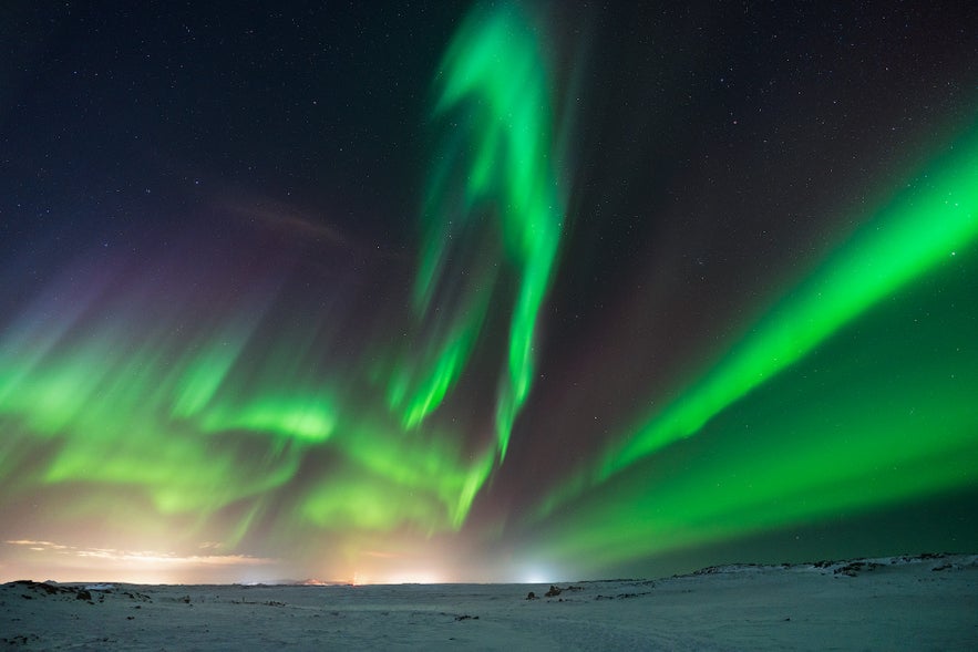 A starry dark sky is brightened by ribbons of green northern lights. 