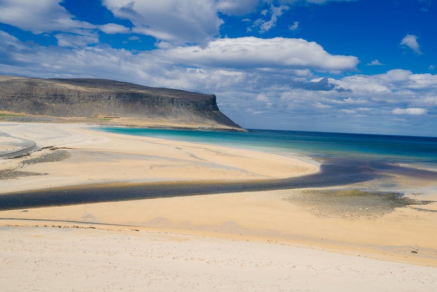 Raudasandur Beach stretches under a blue, cloudy sky in Iceland's Westfjords.