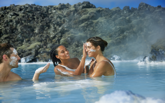 Two people relaxing in the Blue Lagoon’s geothermal waters surrounded by lava rocks.