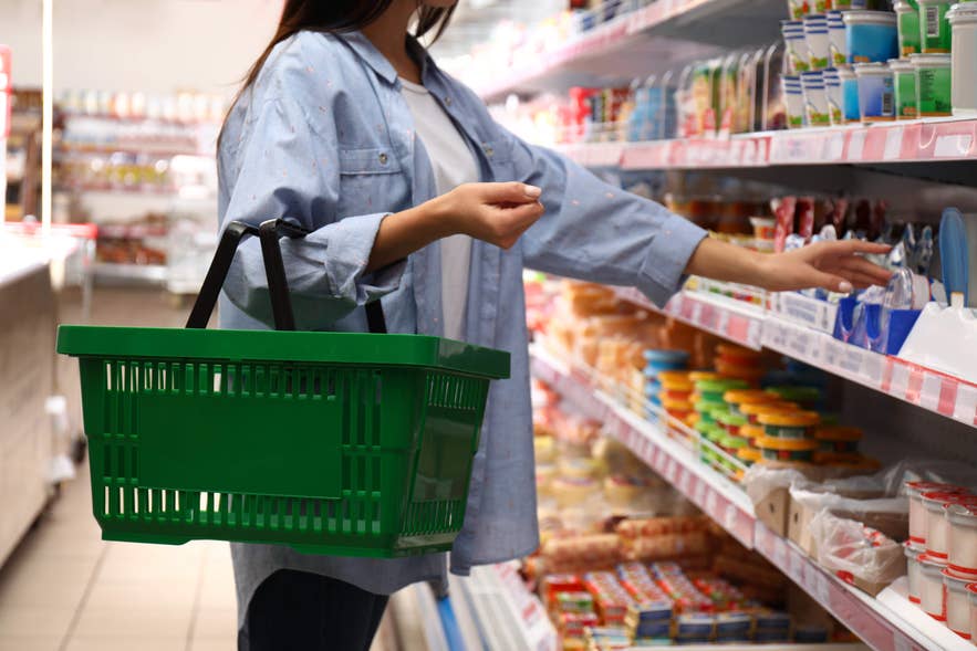 A person holding a green basket while browsing shelves in an Iceland grocery store, showcasing fresh products and essentials.