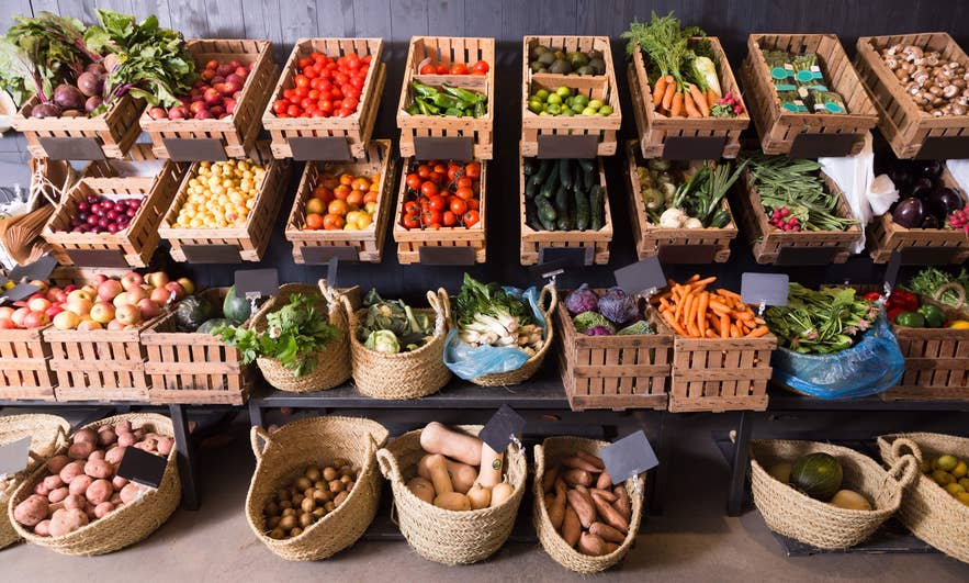 Fresh vegetables and fruits displayed in wooden crates at an Iceland grocery store, showcasing local produce for shoppers.
