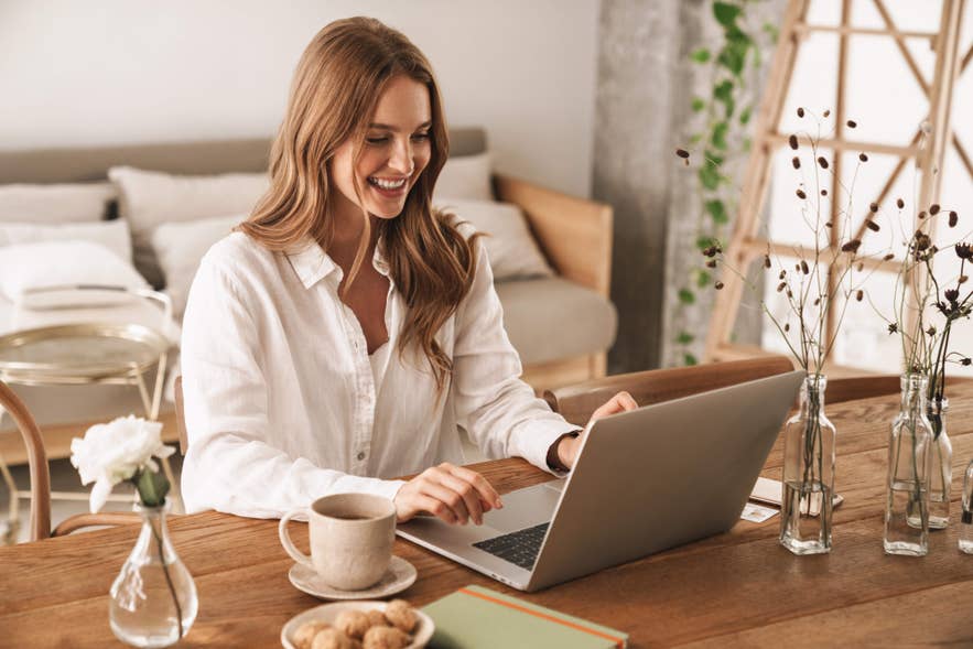 A person smiling while using a laptop at a bright indoor workspace, researching volunteer programs