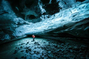 Explorer in red jacket stands inside Solheimajokull ice cave, beneath shimmering blue glacier walls in south Iceland.