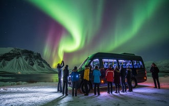 Группа туристов фотографирует северное сияние, стоя у фургона на заснеженном поле.