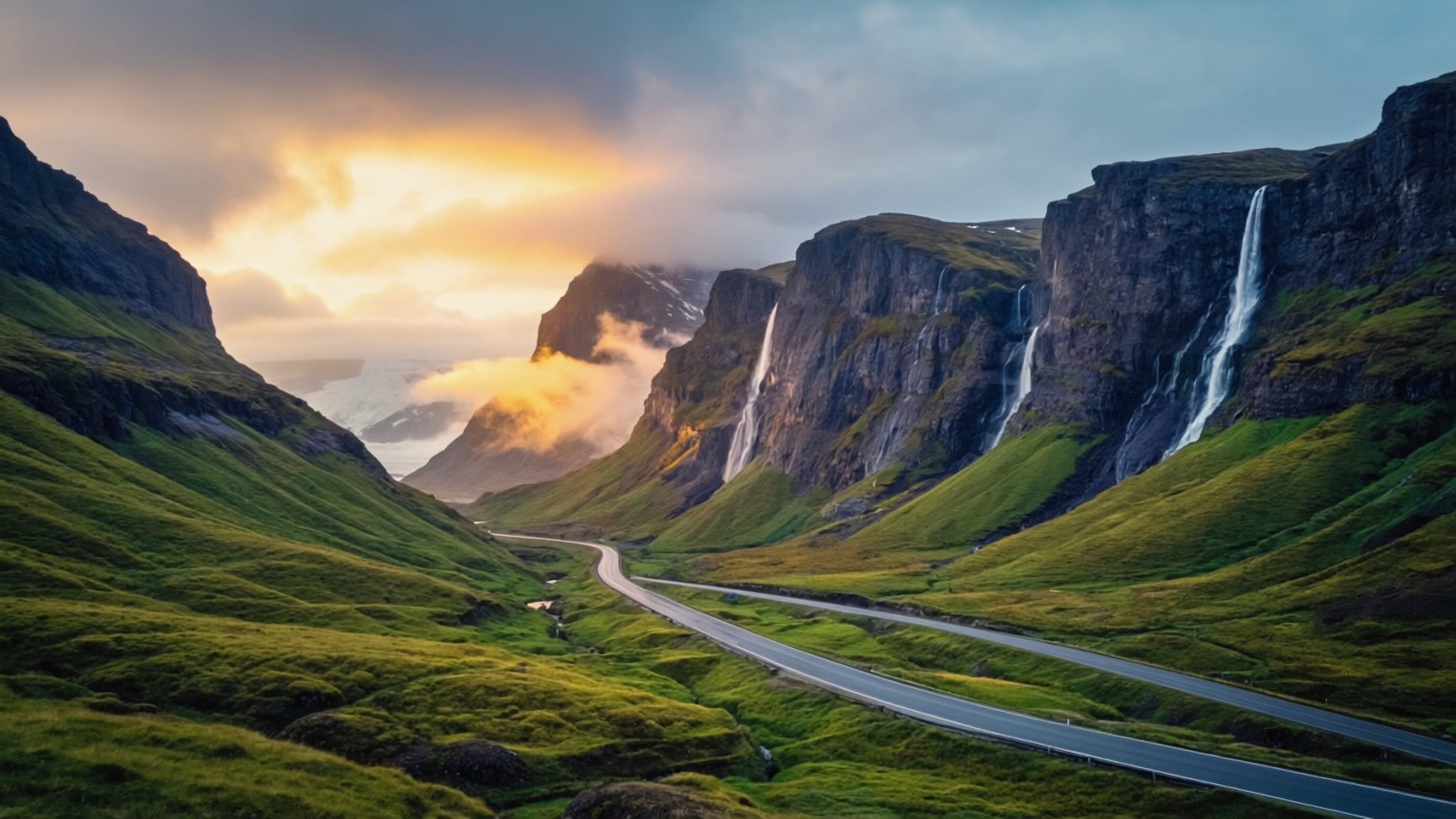 Two paved roads in Iceland appear to converge in the distance, winding through a landscape of lush greenery with towering mountains in the background.