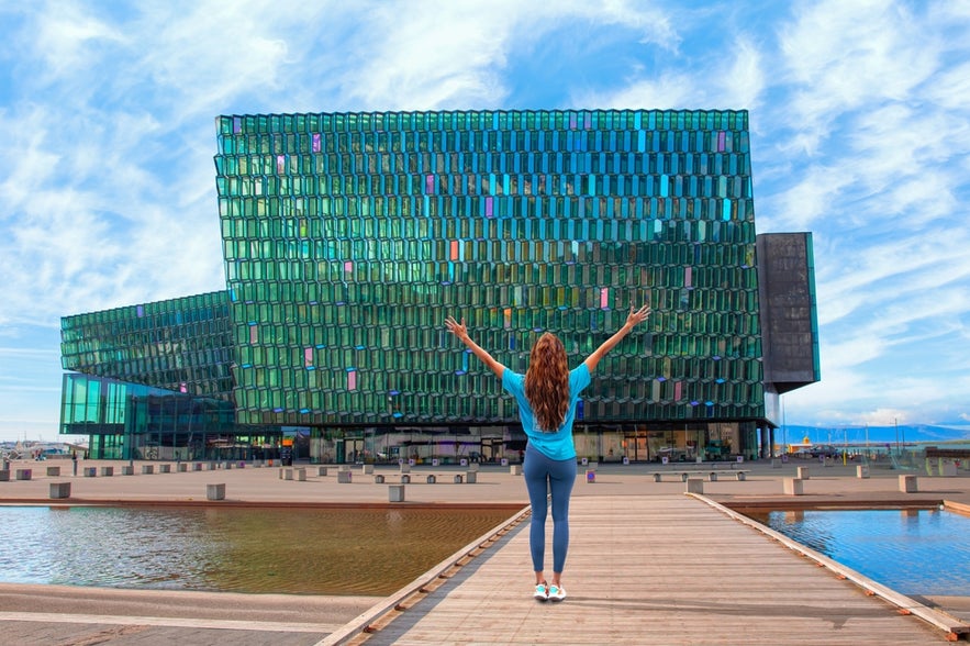 A visitor standing by Reykjavik harbor with Harpa Concert Hall in the background.