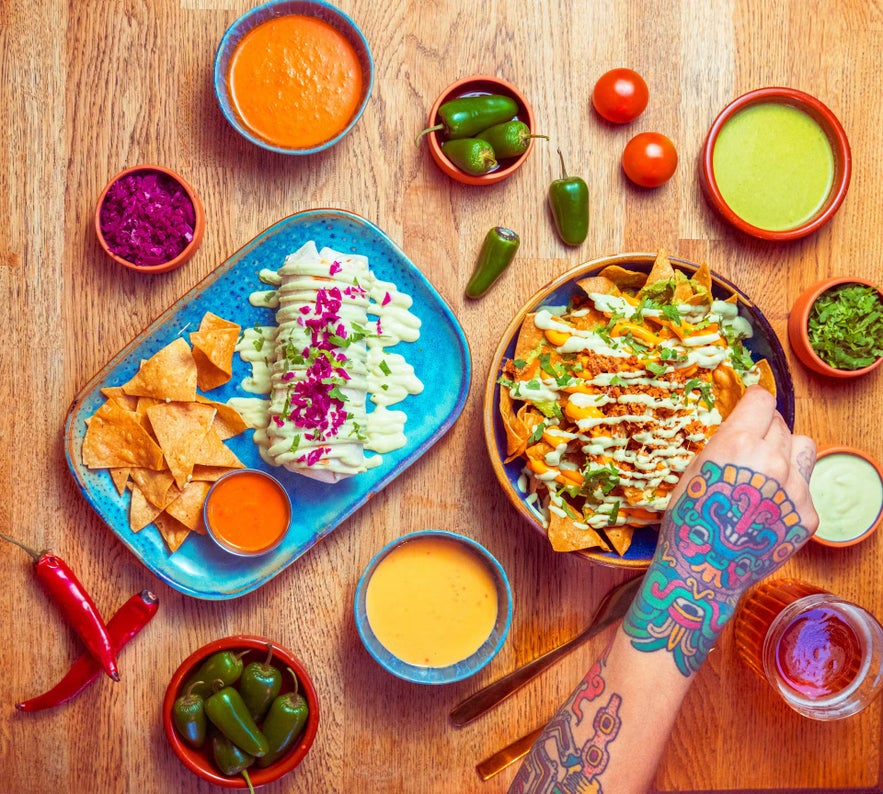 Top view of colorful Mexican dishes at La Poblana in Reykjavik, including tacos, nachos, and salsas on a wooden table.